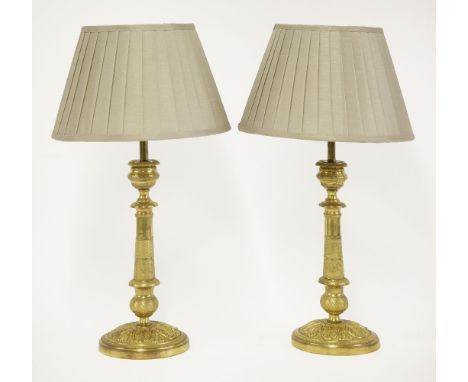 A pair of gilt metal candlesticks,with cast engine turned decoration, converted into table lamps complete with shades,35cm hi