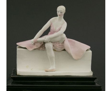 A Chelsea Cheyne figure,a ballerina seated on a bench, with one leg crossed over her other leg, mounted on a stepped wooden p