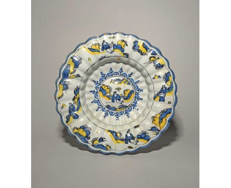 A fluted delftware charger, c.1690, painted in blue, black and yellow with a Chinese figure seated in a garden, the wide rim 