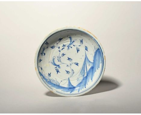 An unusual delftware dish, mid 18th century, painted in blue with a tent-like structure flying a flag beneath a tall flowerin