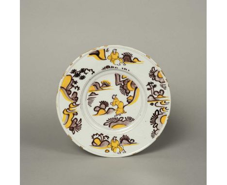 A rare delftware plate, late 17th century, painted in yellow and manganese with a Chinese figure in a landscape, the rim with