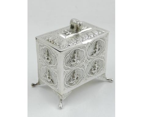 An Indian white metal tea caddy, the lid with elephant finial, overall with embossed carouches depicting seated deities, rais