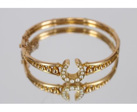 A 15 carat gold snap bangle, with pierced and beaded decoration with central seed pearl set horseshoe motif