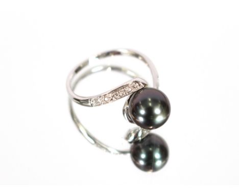 A 14 carat white gold ring, set with a central black pearl between diamond shoulders