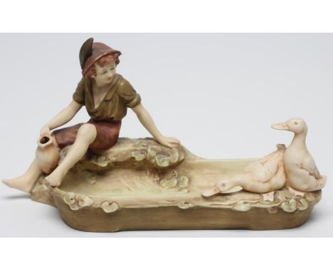 A ROYAL DUX FIGURAL SMALL CENTRE BOWL, early 20th century, the young peasant boy holding a pitcher and seated on the edge of 
