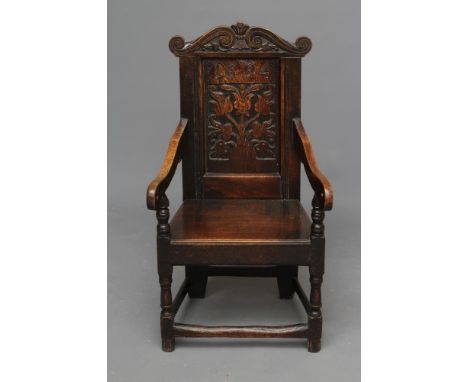A JOINED OAK ARMCHAIR, c.1700, the panelled back carved with tulips and dated "1694" below and a boldly scrolled cresting, do