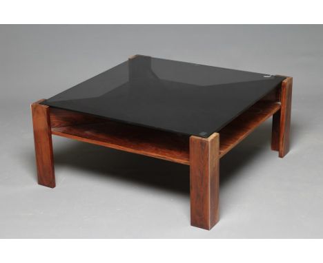 A ROSEWOOD VENEERED COFFEE TABLE, 1970s, of square X form with inset smoke glass top, raised on four square legs with steel e