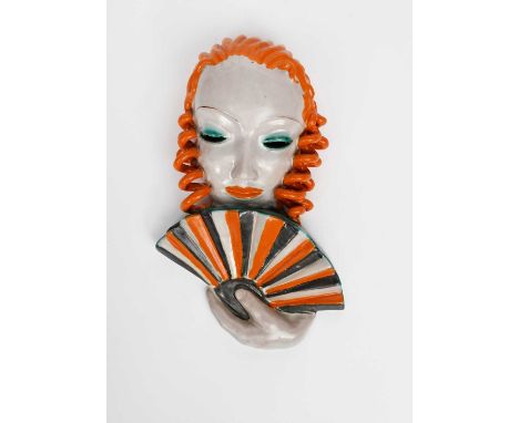 A Goldscheider Pottery wall mask, model no.6542, model as a woman with stylised features and orange hair, holding a fan to he
