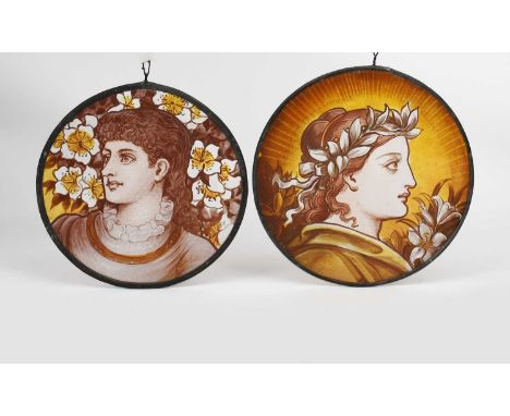 A pair of Arts and Crafts stained glass roundels, each painted with a maiden portrait before flowers, in colours, unsigned, 1