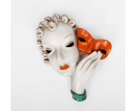 A Goldscheider Pottery wall mask, model no. 7081, modelled as a woman with stylised features, holding an orange mask, in colo