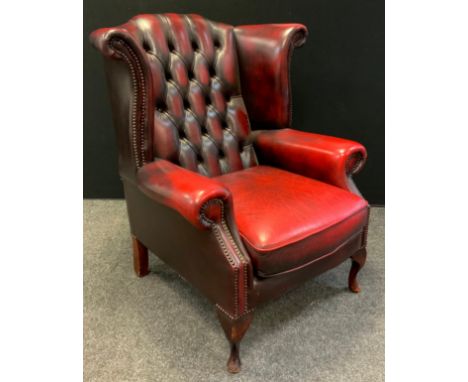 A Chesterfield wing-back armchair, deep button back, sang de bouef red leather, cabriole legs, 102cm tall (45cm to seat) x 83