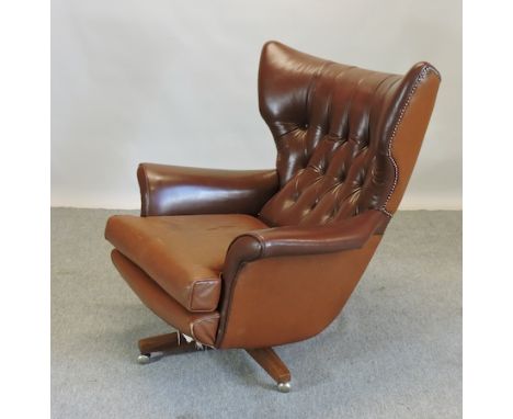 A 1970's style brown upholstered button back swivel arm chair, on a wooden base