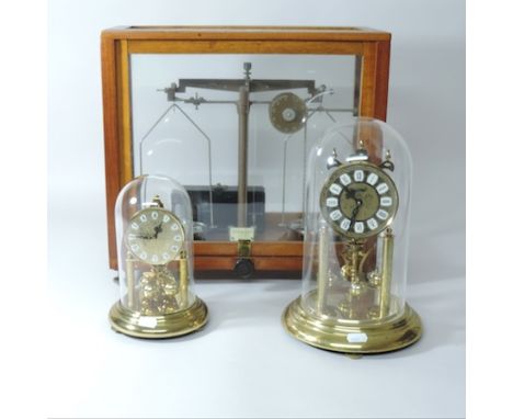 An anniversary clock, contained under a dome, together with another and a set of balance scales, 40cm tall