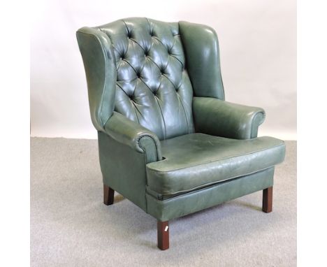 A green leather button back wing armchair, on square legs