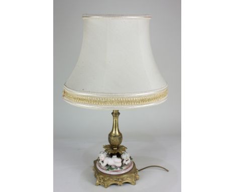 A gilt metal table lamp with leaf cast baluster stem resting on three porcelain recumbent putti, on shaped base, 32cm