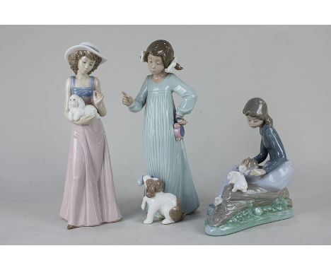 A Nao porcelain figure of a girl seated on a tree stump, with three rabbits, 19cm, together with two others of ladies with do