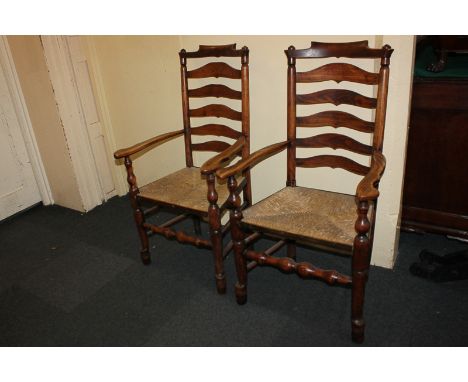 A pair of ladder back carver dining chairs with rush seats, turned legs and stretcher