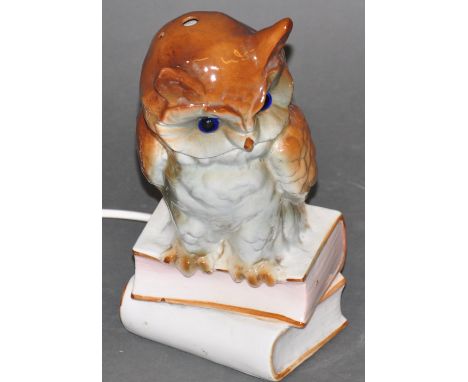 A child's glazed ceramic bedside lamp, modelled as an owl, with blue glass eyes, perched upon books, H. 26cm