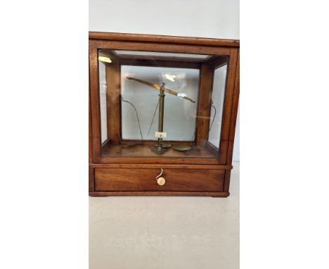 Antique brass balance scale in a glazed mahogany case, from the early 20th century. Features a fitted lower drawer for weight