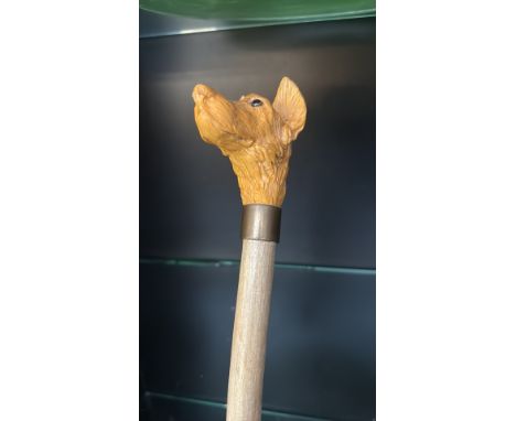 Vintage walking cane with a carved dog’s head handle, from resin or bone, mounted on a wooden shaft with a metal collar.