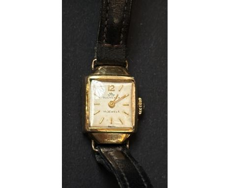 Vintage Bucherer 17-jewel wristwatch with gold-tone case and black leather strap. Square dial with gold indices. Currently ti