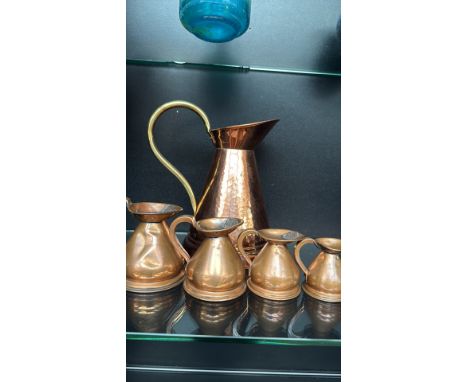 Copper and brass measuring jug set, featuring a large hammered copper pitcher with a brass handle and four smaller lidded mea