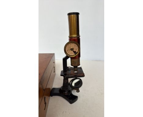 Late 19th-century brass and iron student microscope with adjustable dial, housed in a fitted wooden case. Features a sub-stag