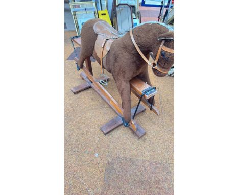 Vintage plush rocking horse with a wooden safety stand, featuring a leather saddle, bridle, and stirrups.