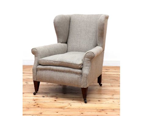 A wingback armchair,early 20th century, upholstered in oatmeal linen, raised on tapering square supports, terminating in cera