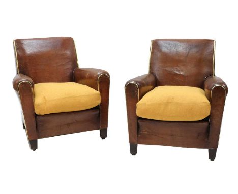 A pair of French leather club chairs,20th century, each with a yellow upholstered cushion and brass piping, raised on short t