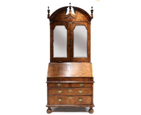 A walnut bureau bookcase,early 18th century, with a break arch pediment and star inlaid reserve, mirrored doors and candle sl