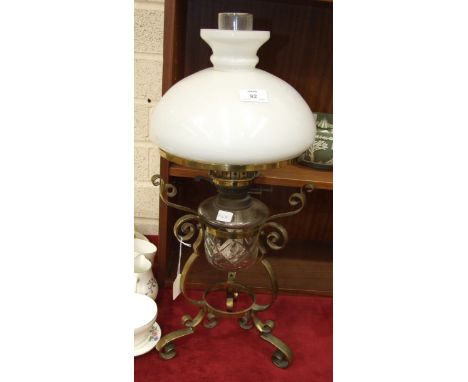 An oil lamp with glass reservoir, on a brass triform stand, with opaque glass shade, 60cm high overall.