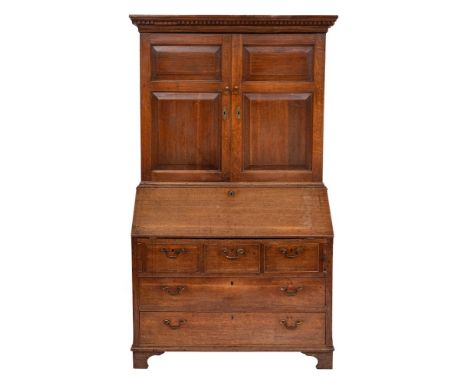 An 18th Century oak bureau cabinet:, the upper part with a moulded dentil cornice, enclosed by a pair of fielded panel doors,