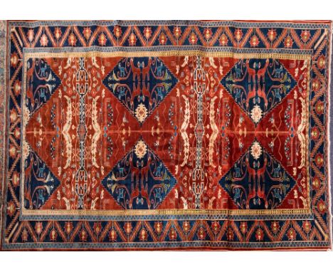 A Persian style carpet:, the brick red field with indigo stepped lozenge medallions with animals and stylised foliate branche
