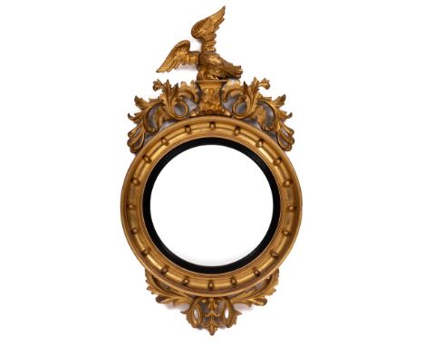 A Regency carved giltwood and gesso circular convex mirror:, the cresting in the form of an eagle on a rocky plateau, flanked