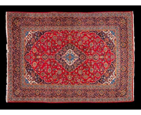 A Kashan carpet:, the red cartouche field with a central indigo stepped and shaped lozenge pole medallion, all over palmette 