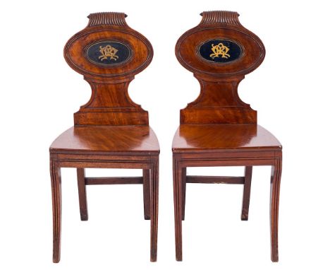 A pair of Regency mahogany hall chairs:, the reeded oval panel backs with painted monograms and reeded scroll crestings, havi