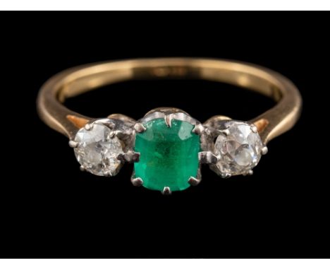 An 18 carat gold emerald and diamond ring,: the central oval cushion cut emerald claw set between two old brilliant cut diamo