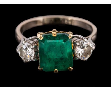 An emerald and diamond ring,: the rectangular cut emerald claw set between two brilliant cut diamonds, approximately 0.75 car