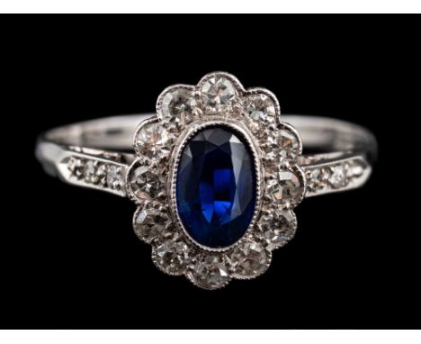 A sapphire and diamond ring,: the central oval cut sapphire collet set within a surround of eight cut diamonds, between eight