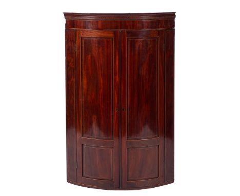 An early 19th Century mahogany and inlaid bow-fronted hanging corner cupboard:, bordered with boxwood and ebonised lines, hav