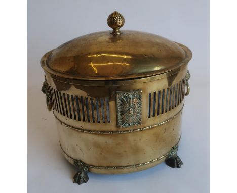 Regency style brass oval fuel bin, vented body with lion mask and ring handles, domed cover with leaf cast finial, on four pa