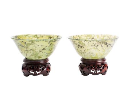 A pair of Chinese jade finger bowls of plain circular form with mottled inclusions, with polished wood stands, 10cm diameter,