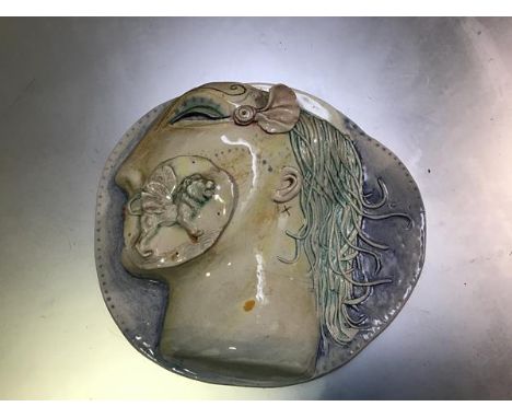 Claire Gordon, Head wall piece, a moulded plaque with applied winged lion patch, inscribed verso and signed '81(h.4cm x 23cm 