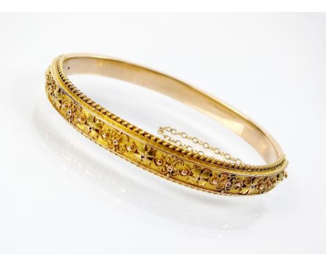 A late 19th century yellow metal hinged bangle, designed as a decorative band of scroll work within rope twist border, the cl