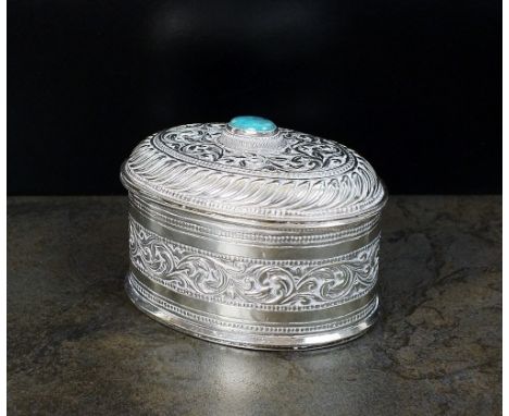 A white metal oval box and cover, with chased decoration, the hinged cover with cabochon turquoise finial, stamped to the bas
