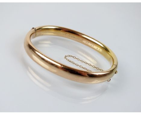 A yellow metal hollow hinged bangle, with engraved presentation inscription, stamped '15ct', weight 15.4gms