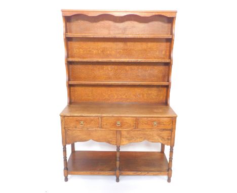 A Georgian style oak dresser, with a three shelf plate rack, over three frieze drawers, raised on turned legs with a shaped a