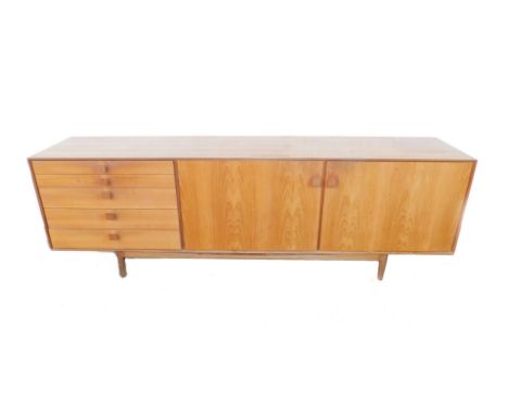 A 1960's teak sideboard, with a pair of doors enclosing a single shelf, flanked to the left by five drawers, raised on turned