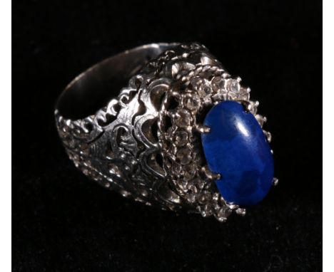 White metal openwork ring set with central blue cabochon encircled by a band of diamonds, the shank stamped 750, size K, 7.7 